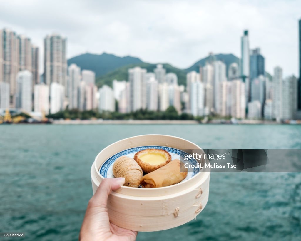 Hand Holding a Basket of Dim Sum Against City Skyline