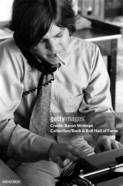 Portrait of Jann Wenner, founder and publisher of Rolling Stone magazine, taking a phone call, smoking and typing at a typewriter in the magazine's...