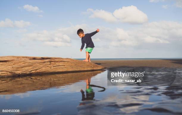 kid balancing up himself on log at beach. - new zealand farmer stock pictures, royalty-free photos & images