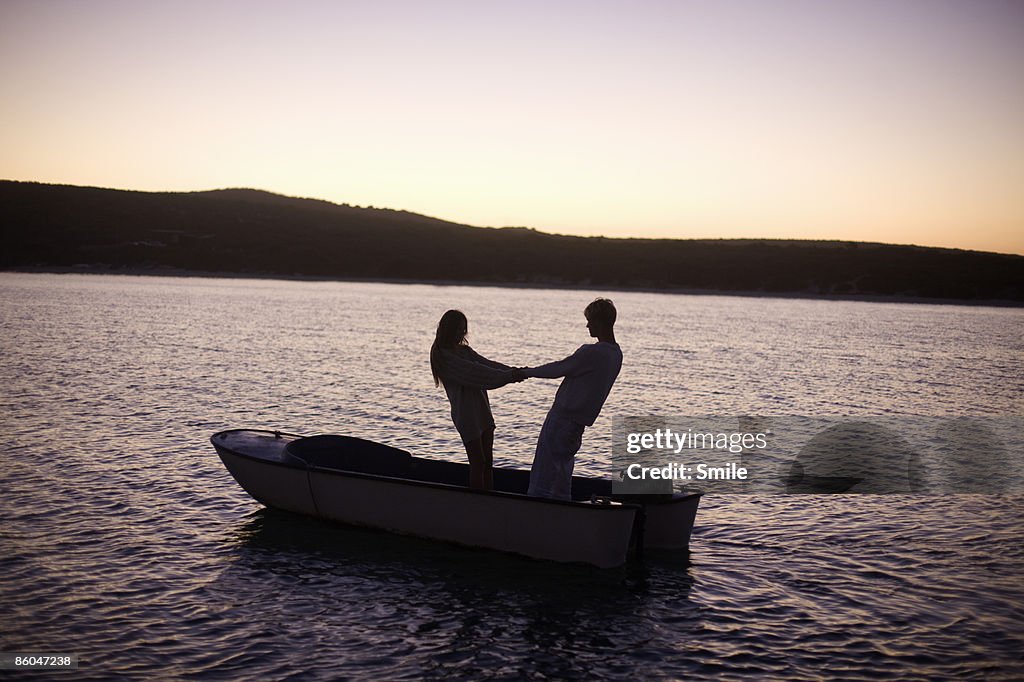 Couple holding hands on dinghy at sunset