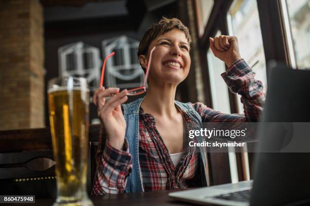 happy woman using laptop in a bar and celebrating good news. - punching the air stock pictures, royalty-free photos & images