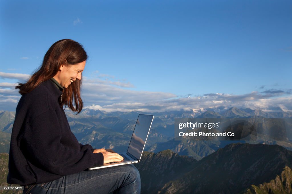 A woman sat on a rock using a laptop