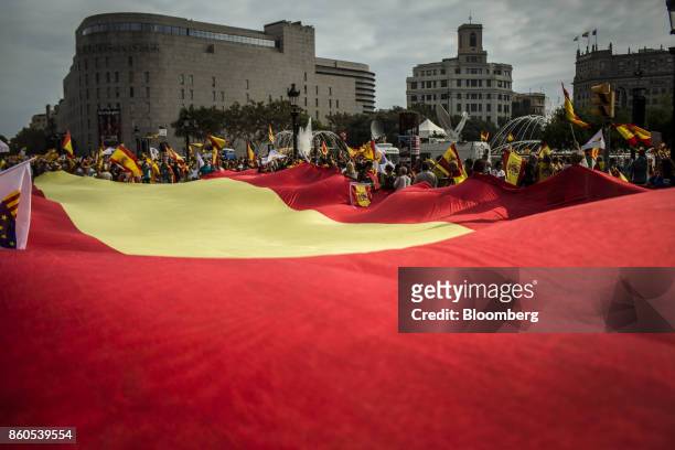 Demonstrators hold a massive Spanish national flag as they gather on Catalonia Square in support of Spanish unity during a march on Spain's National...