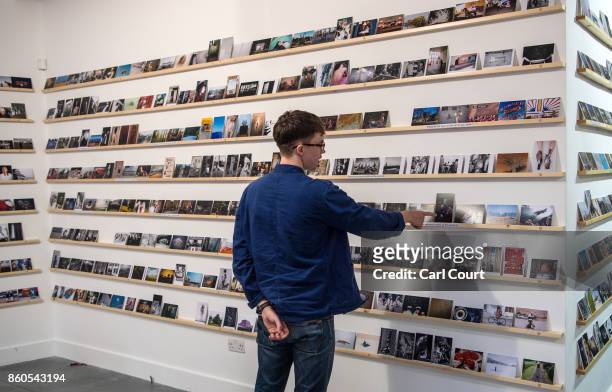 Member of staff gestures as he poses next to photograph postcards featuring images by photographers including Martin Parr and Wolfgang Tillmans ahead...