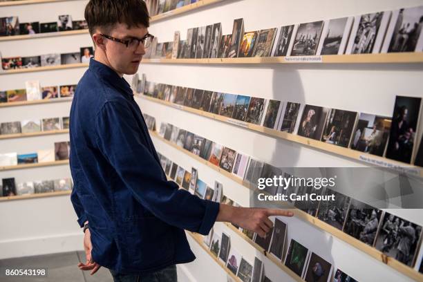 Member of staff gestures as he poses next to photograph postcards featuring images by photographers including Martin Parr and Wolfgang Tillmans ahead...