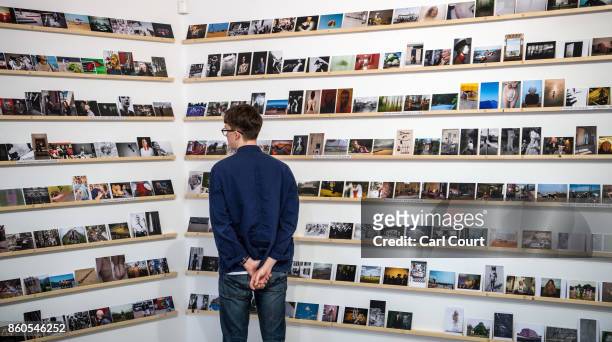Member of staff poses next to photograph postcards featuring images by photographers including Martin Parr and Wolfgang Tillmans ahead of a secret...