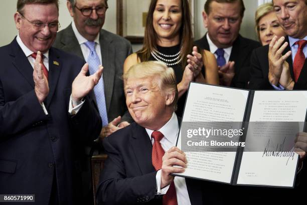 President Donald Trump holds up a signed executive order on health care in the Roosevelt Room of the White House in Washington, D.C., U.S., on...