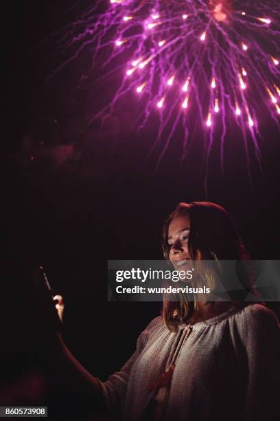 junge frau unter selfies mit feuerwerk am nachthimmel - firework display stock-fotos und bilder