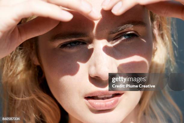 woman shielding eyes from sun - augen zukneifen stock-fotos und bilder