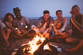 Young multi-ethnic friends roasting marshmallows on sticks at the beach