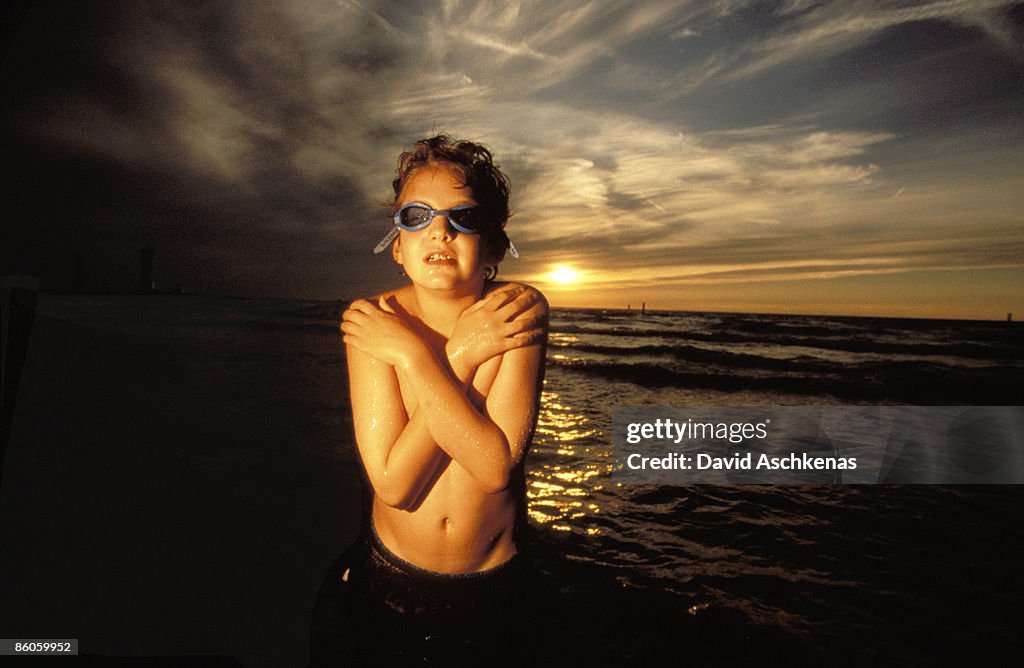 Boy shivering on beach at sunset