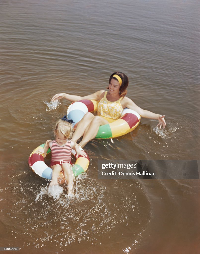 Retro mother and daughter floating in water with inflatable rings