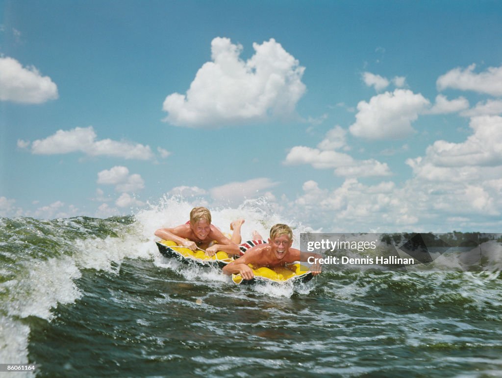 Boys riding waves on inflatable rafts