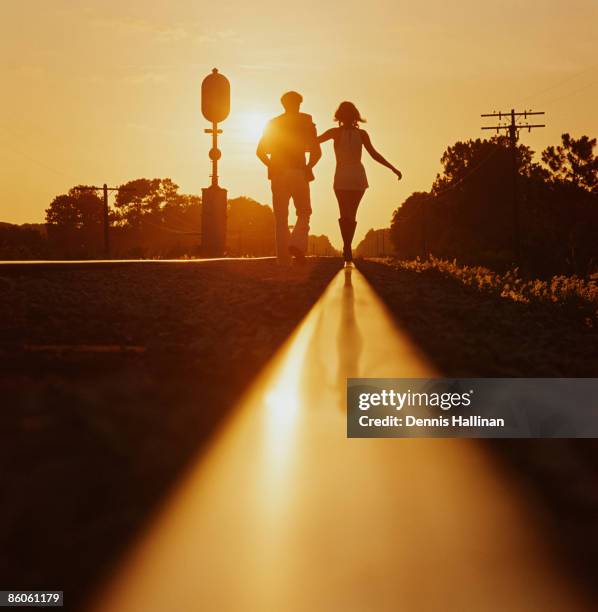 Silhouette of couple walking on railroad tracks at sunset