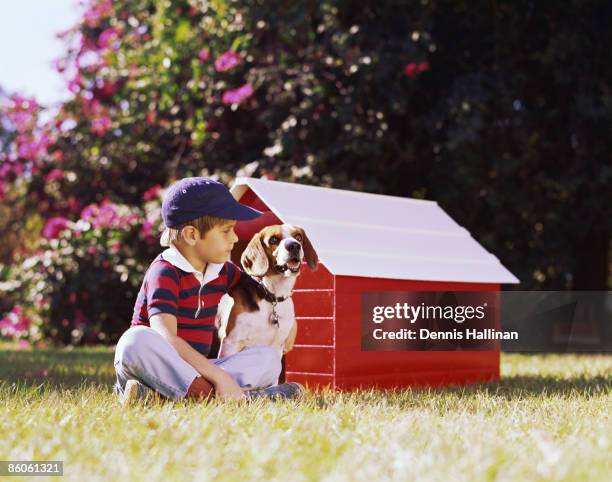 Boy sitting outside with puppy next to doghouse