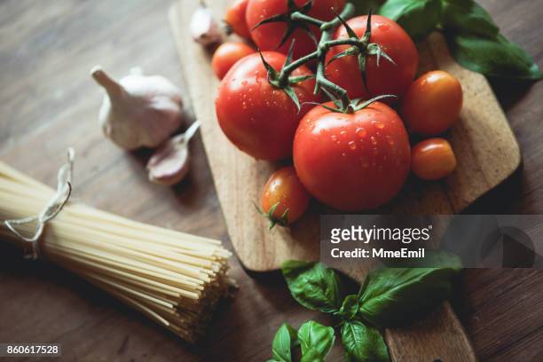 spaghetti, knoblauch, basilikum und tomaten auf einem schneidebrett - zutaten stock-fotos und bilder