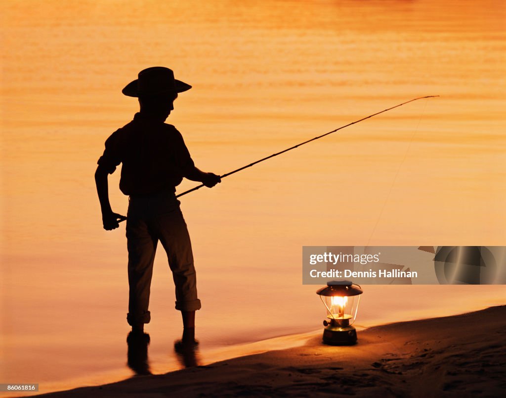 Boy pole fishing by shoreline with an oil lamp