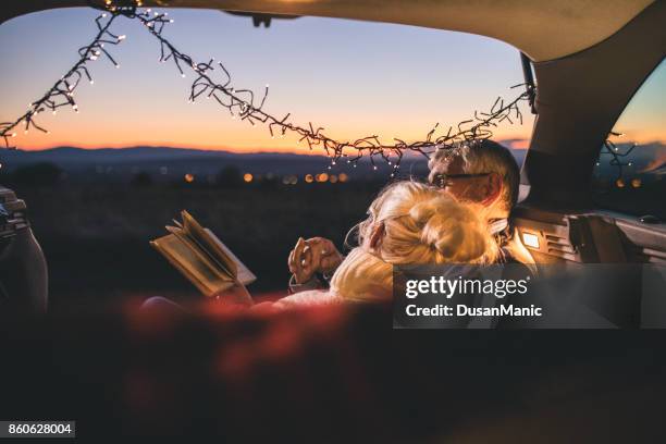 senior couple sit in open car trunk and reading a book - senior reading stock pictures, royalty-free photos & images