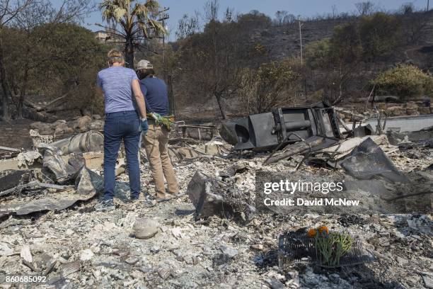 Flowers mark the spot where their father died as sisters Liz and Mimi stand in the ruins of the house of 100-year-old Charles and 98-year-old Sara...