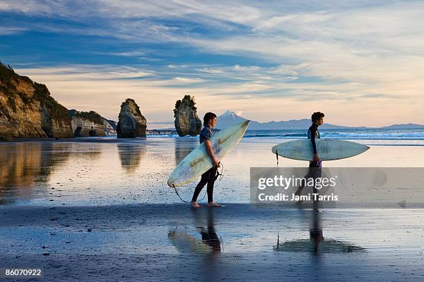 surfers walking on beach, three sisters rocks, north island, new zealand - north island new zealand 個照片及圖片檔