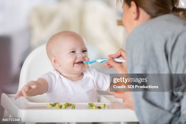 adorable baby in high chair laughs while being spoon fed - baby food stock pictures, royalty-free photos & images