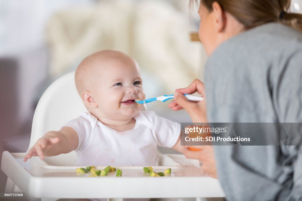 Adorável bebê na cadeira alta ri enquanto sendo colher alimentados