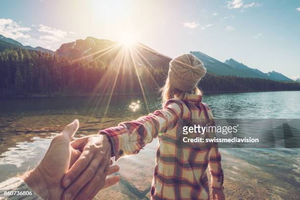 follow me to- young woman leading man to mountain lake at sunrise - follow me to man stock pictures, royalty-free photos & images