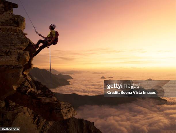 climber on a rocky wall over clouds - alpinismo fotografías e imágenes de stock