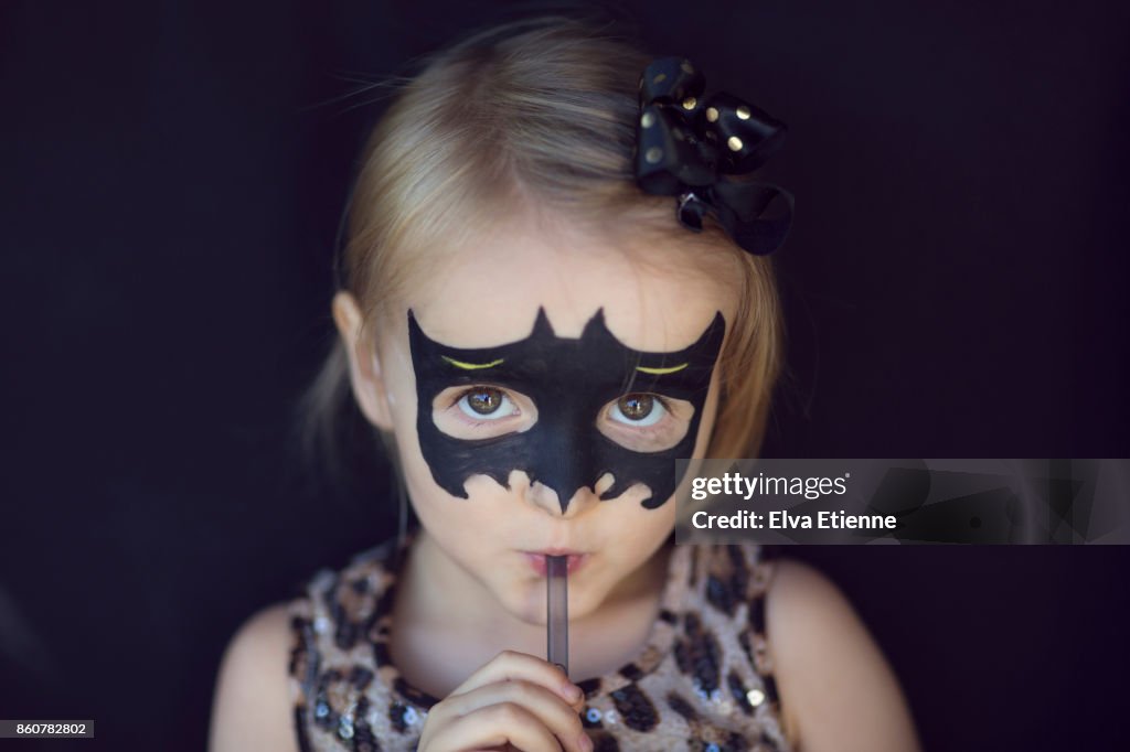 Girl with bat shaped Halloween face paints, drinking through a straw