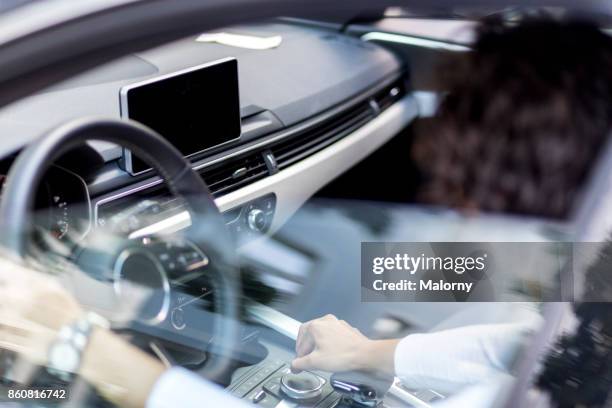 young woman sitting in drivers seat of a black car. using navigation device. - auto innenansicht stock-fotos und bilder