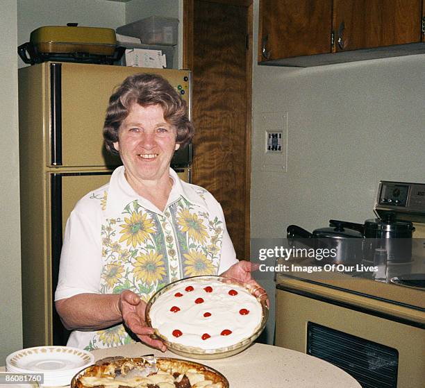 smiling woman in kitchen holding pie - stereotypical housewife stock-fotos und bilder