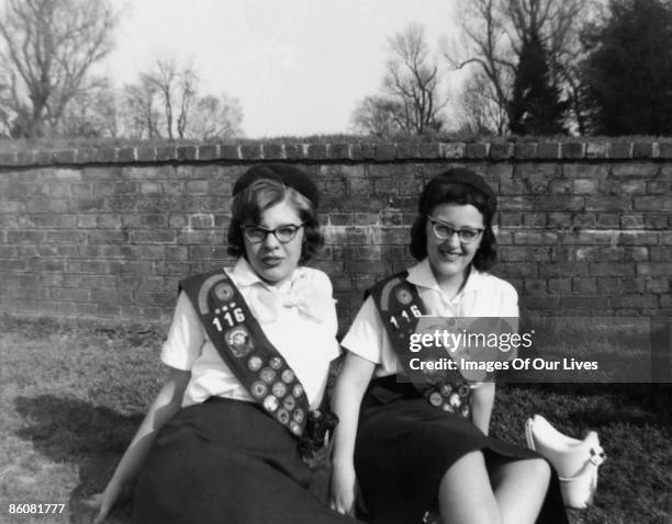 retro girl scouts sitting on the grass by brick wall - girl scout stock-fotos und bilder