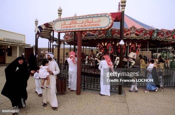 Hommes et femmes en costume traditionnel à côté d'un manège dans le parc d'attractions de l'an 2000 à Koweït City en mai 1984, Koweït.