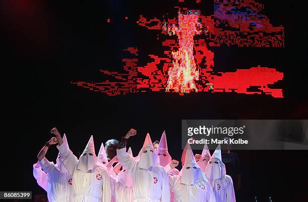 Performers in the Klu Klux Klan dance number stand on stage in front of a big screen displaying a burning cross during the "Jerry Springer: The...