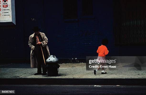 Little girl in a red cardigan passes a man on a street in New York City, August 1962.