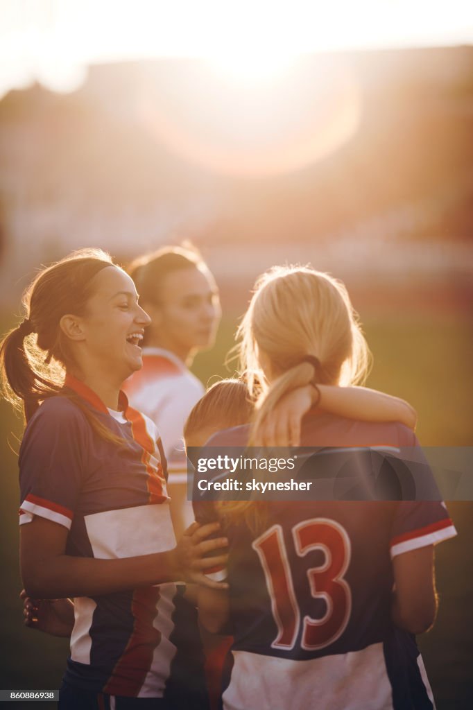 Fröhliche Teenager Fußball-Spieler lachend auf einem Spielfeld bei Sonnenuntergang.