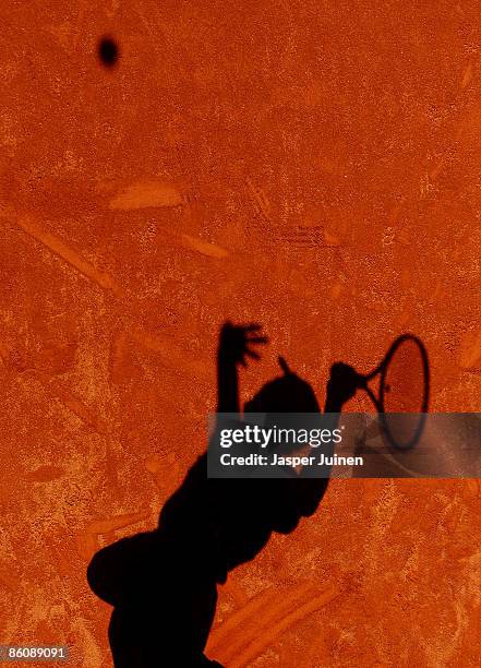 Nikolay Davydenko of Russia cast his shadow in the gravel as he serves the ball during his doubles match with his fellow countryman and doubles...