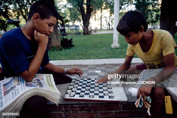 Deux jeunes vendeurs de journaux jouent aux dames avec des capsules de bouteille dans un parc en avril 1982 à Asuncion, Paraguay.