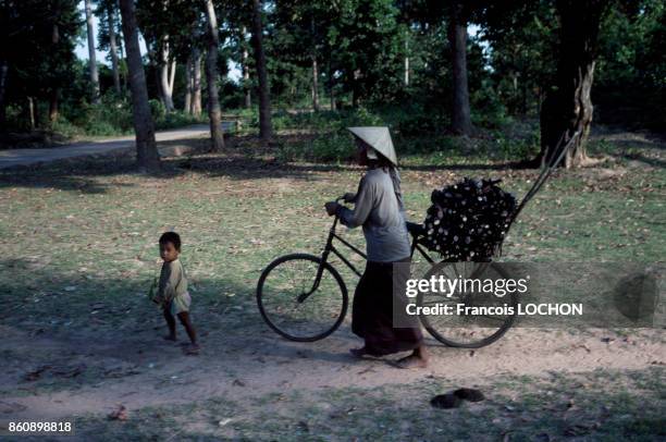 Une femme avec son enfant pousse son vélo sur lequel elle transporte du bois en mai 1991, Cambodge.