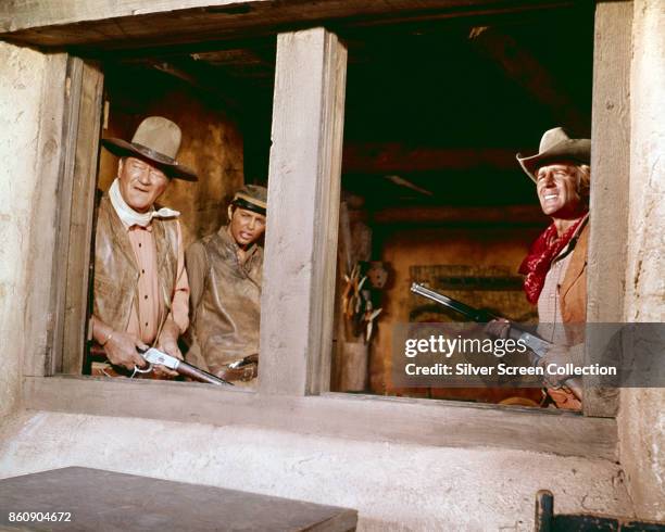 American actors John Wayne and Christopher Mitchum , both with rifles, as they look out of a window in a scene from 'Rio Lobo' , 1970. The actor in...