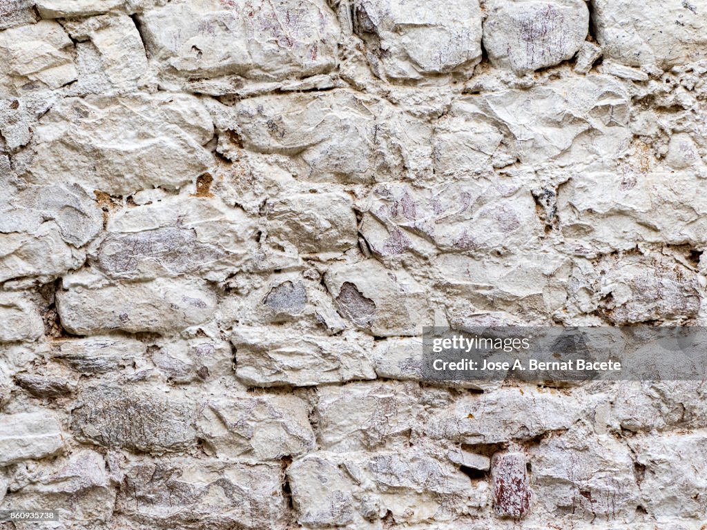Complete setting of a facade of a cement wall with stones of white colors, ancient and spoil in the time