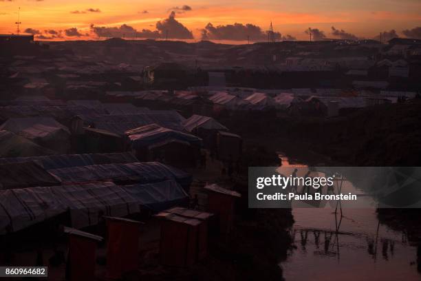 People cross a bamboo bridge over a stream as the sun sets on October 13, 2017 at the Kutuplaong refugee camp, Cox's Bazar, Bangladesh. According to...