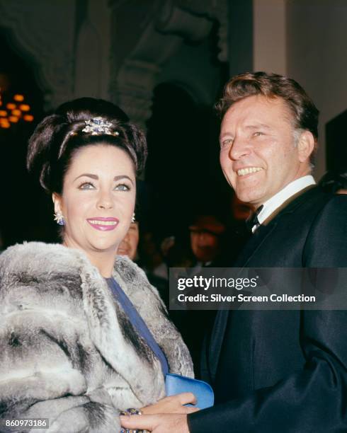 Low-angle portrait of married actors Elizabeth Taylor and Richard Burton as they attend the premiere of the latter's film, 'The Spy Who Came in from...