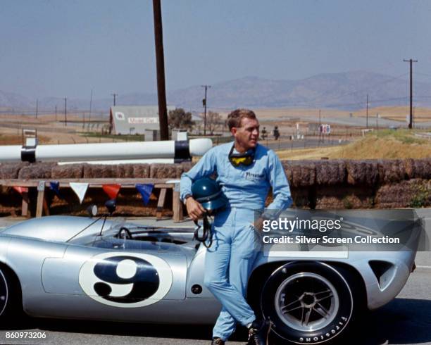 American actor Steve McQueen , in Firestone racing suit, leans against a Lola T70 SL70/14 car at Riverside Raceway, Riverside, California, July 1966.