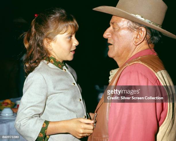 American actor John Wayne talks with his daughter Aissa in an unspecified restaurant, 1967. Wayne is in costume for his role in 'El Dorado' .