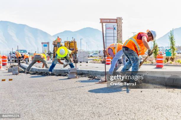 road construction worker scoups up concrete while cleaning up a center medium just laid in spanish fork, utah. other workers smooth out the center medium with a float - road construction stock pictures, royalty-free photos & images