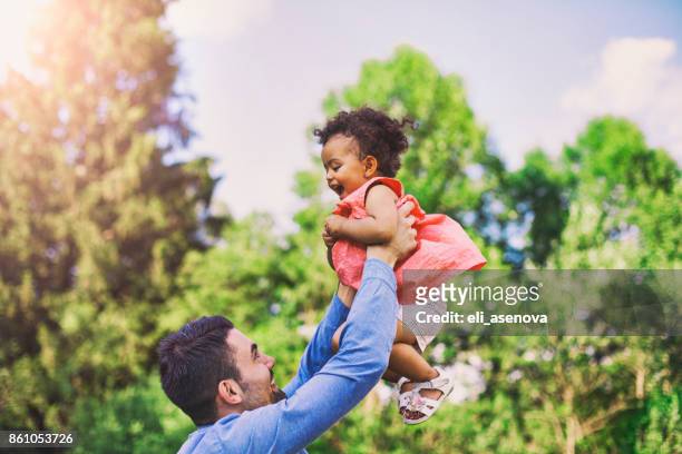 vader zijn baby dochter gooien in de lucht in een park - dad throwing kid in air stockfoto's en -beelden