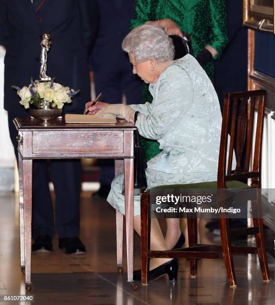 Queen Elizabeth II signs a visitors book as she attends a reception to mark the Centenary of the Women's Royal Navy Service and the Women's Auxiliary...