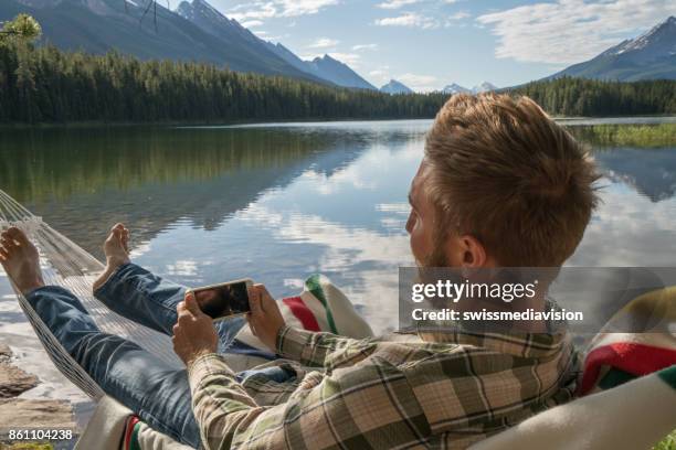 young man relaxing on hammock with smart phone - smartphones dangling stock pictures, royalty-free photos & images