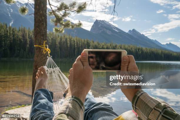 personal perspective of young man relaxing on hammock and using mobile phone - smartphones dangling stock pictures, royalty-free photos & images